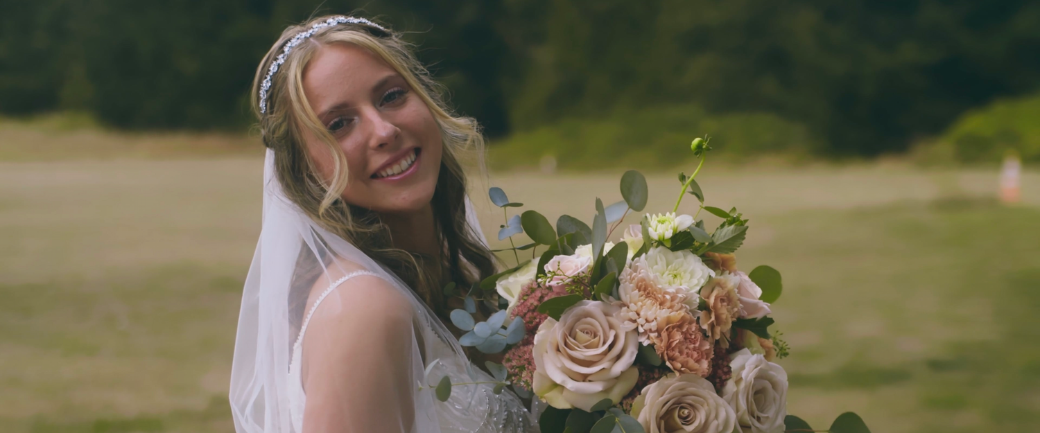 Smiling bride in white veil holding a beautiful bouquet of pink and white flowers.