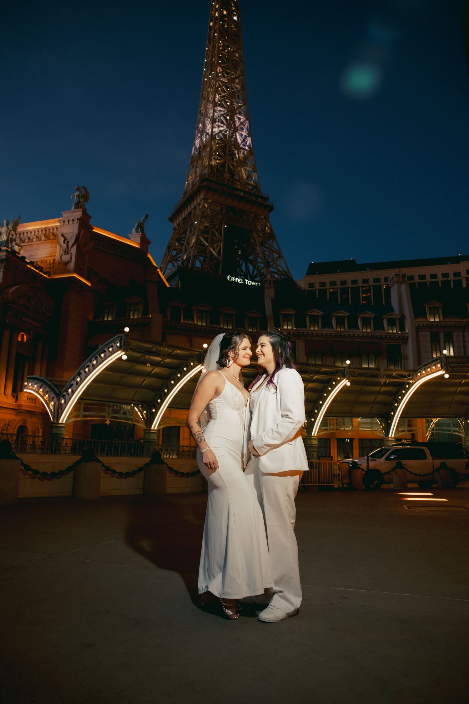 Two brides pose romantically at night in front of the Paris Las Vegas Eiffel Tower replica.