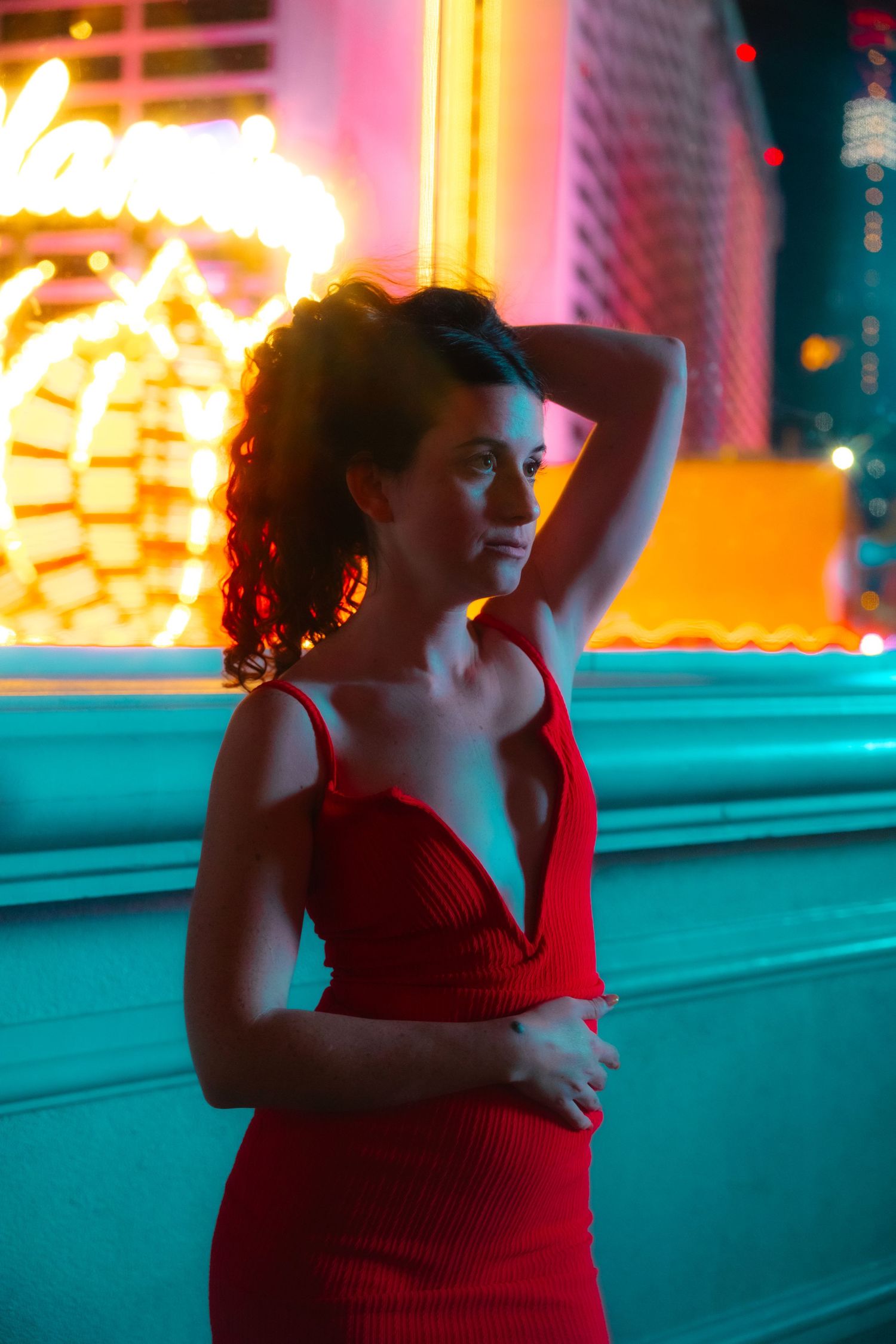 Woman in red dress poses under colorful neon lights on the Las Vegas Strip at night.