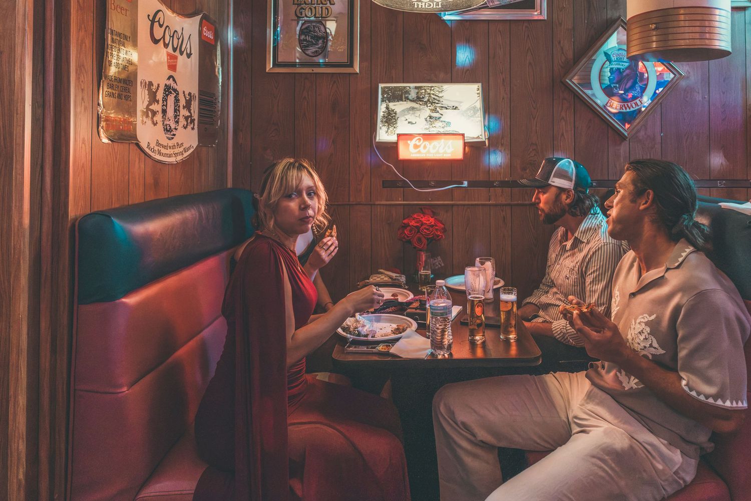 Three people dining in a cozy retro diner booth with red leather seats and vintage decor.