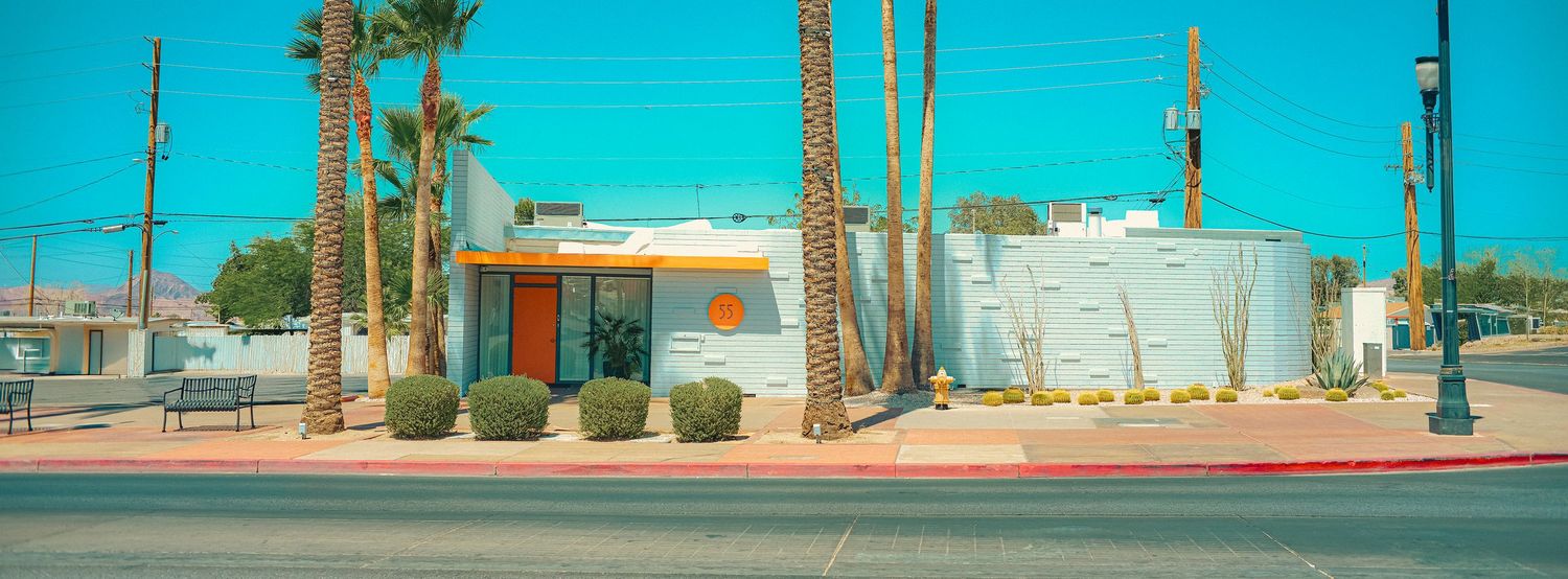 A retro mid-century modern building with palm trees and desert landscaping on a sunny day in the American Southwest.