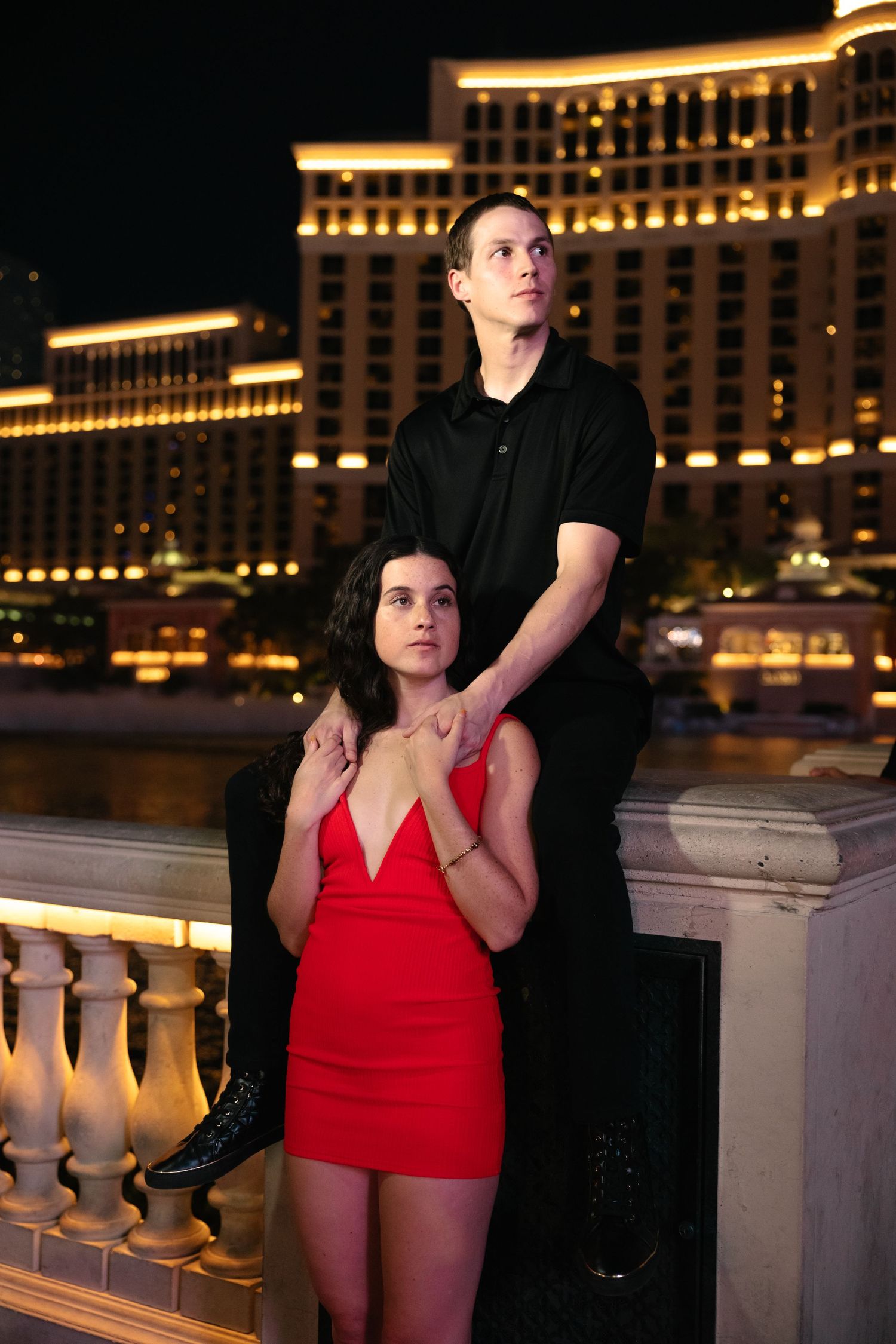 Couple posing at night near Bellagio Las Vegas, woman in red mini dress, man in black shirt behind her.