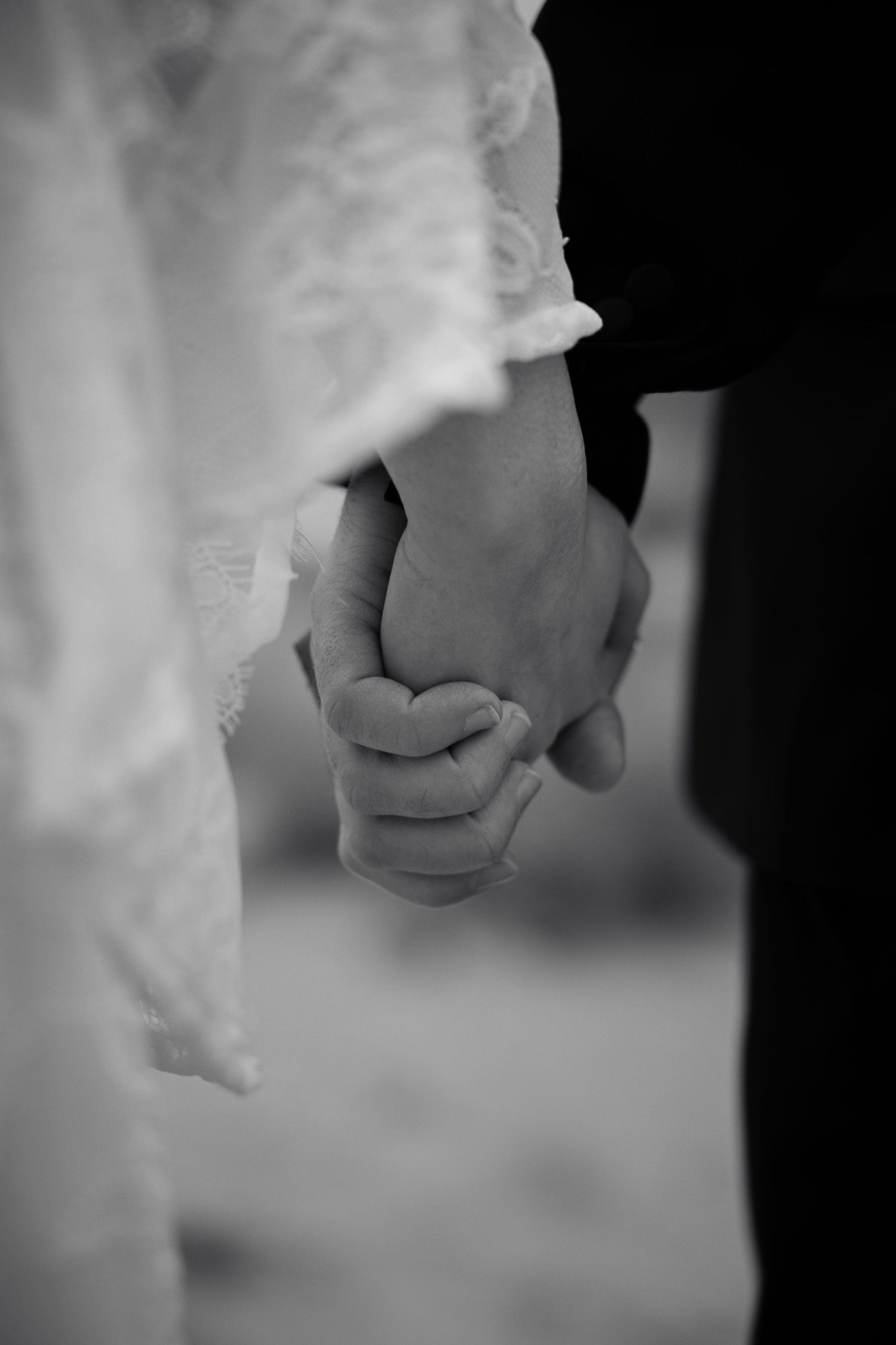 Black and white close-up of bride and groom holding hands during their wedding ceremony outdoors.