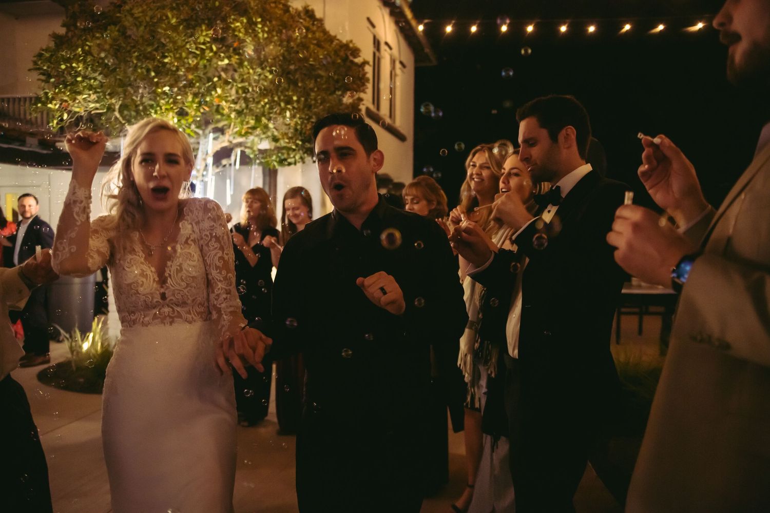 Bride and groom dance and celebrate with guests during outdoor nighttime wedding reception.