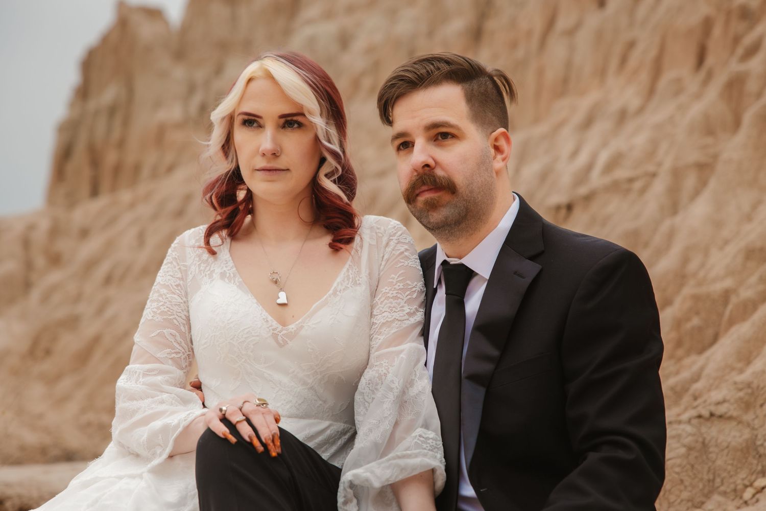 Close-up portrait of bride and groom sitting together against sandy desert rock formation backdrop.