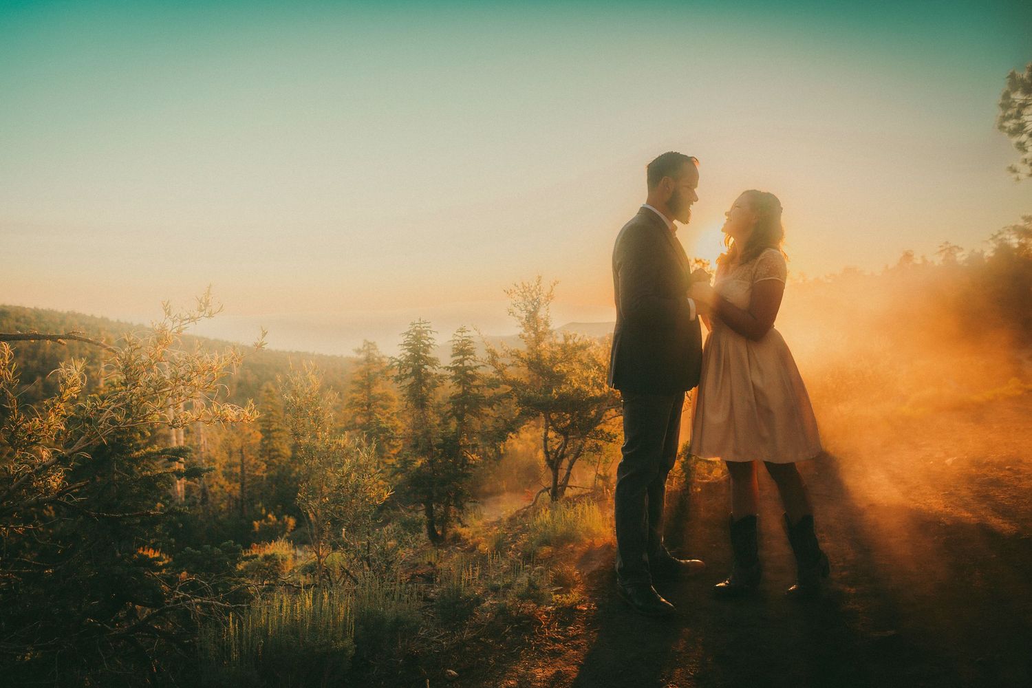 Couple standing together at golden sunset on a hilltop surrounded by glowing mist and autumn foliage.