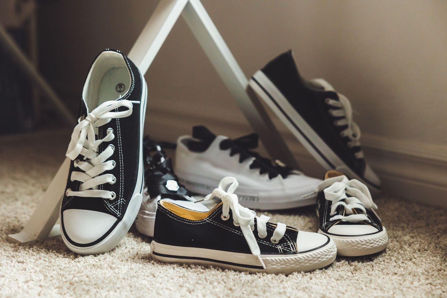 Multiple pairs of black and white Converse sneakers in various sizes arranged on a carpet floor.