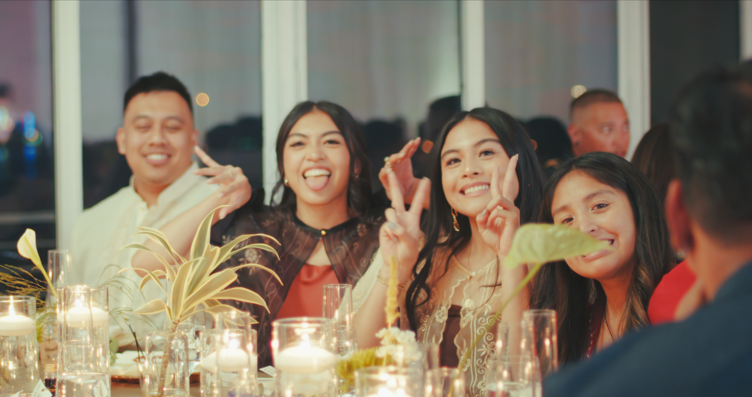 Guests smiling and posing at a wedding reception dinner table with candles and floral centerpieces.