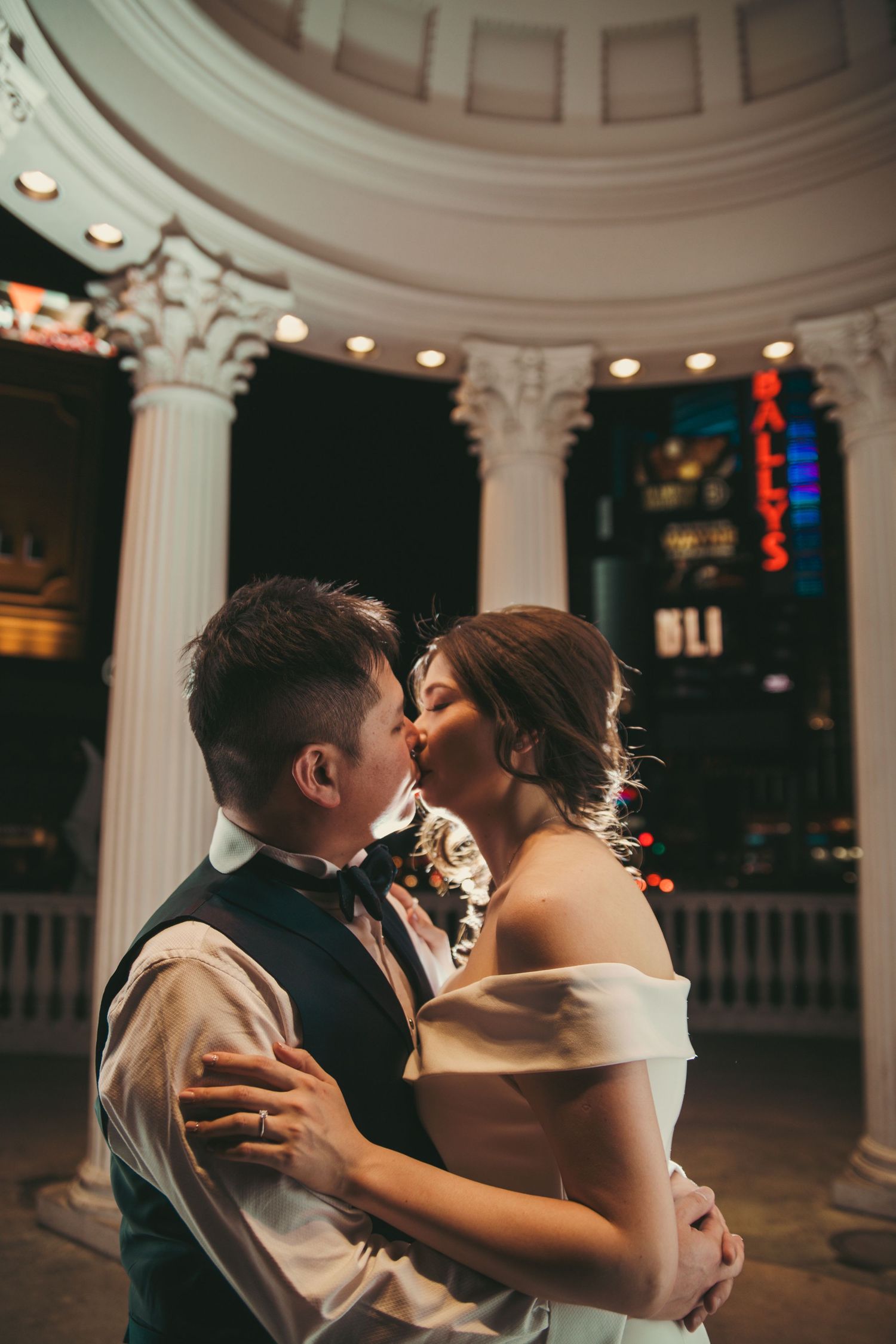 Bride and groom share a romantic kiss outside Ballys Las Vegas at night.