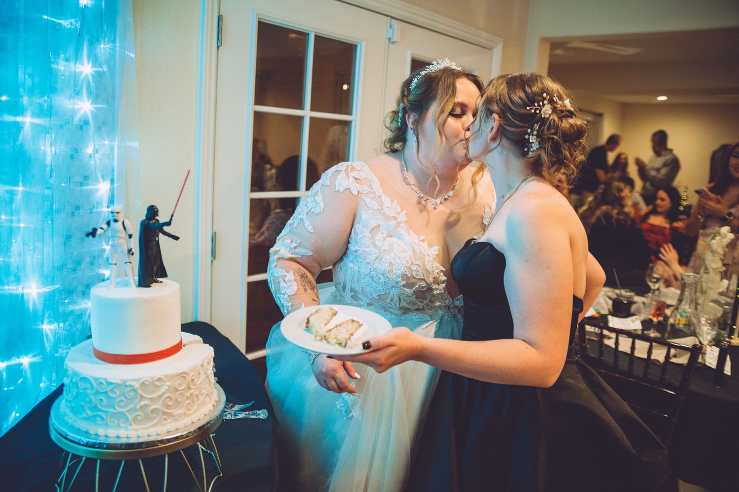 Two brides share a kiss while cutting their Star Wars themed wedding cake at their reception.