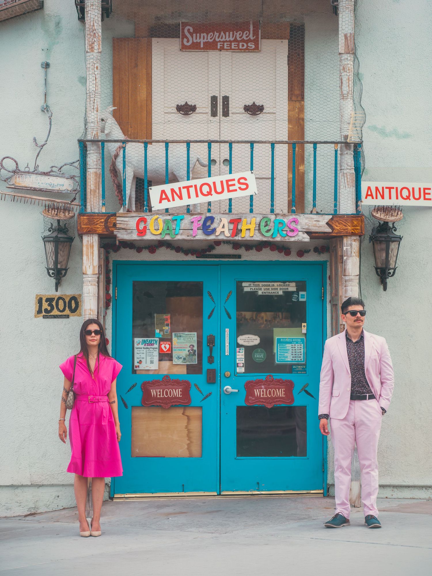 Couple in pink outfits posing outside a colorful antiques shop with turquoise doors at 1300.