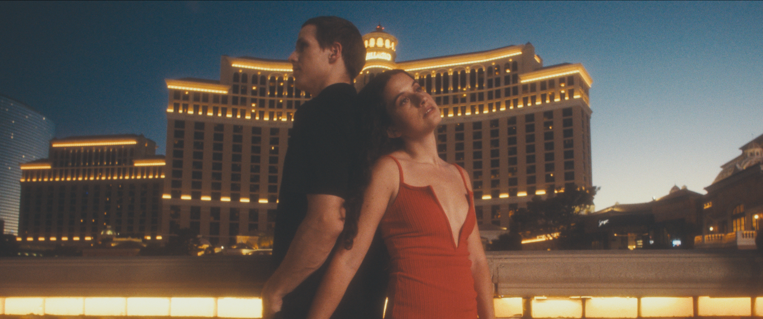 Couple standing back-to-back in front of the illuminated Bellagio hotel in Las Vegas at dusk.