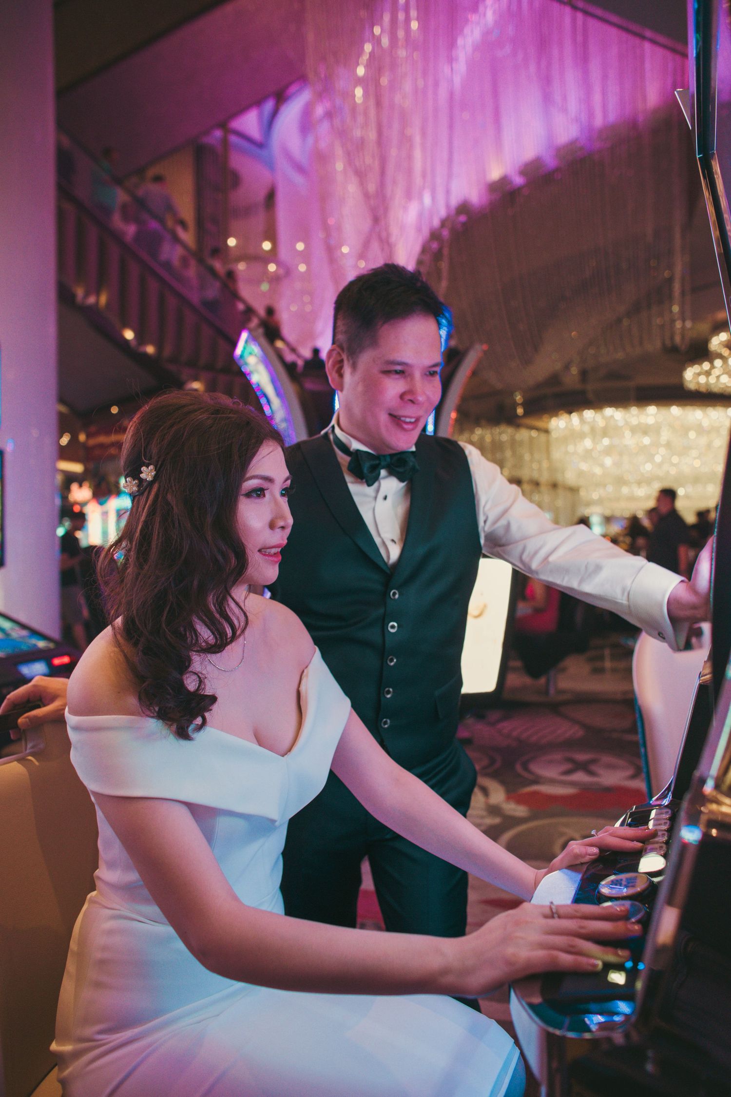 Bride and groom playing slot machines together at a casino on their wedding day.