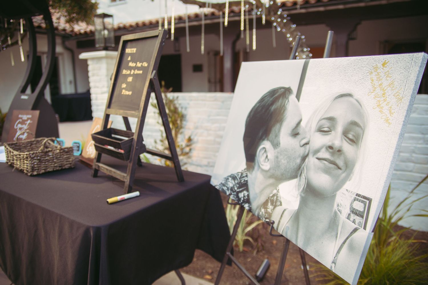 Wedding guest book display with large black and white couple photo on easel at outdoor reception.