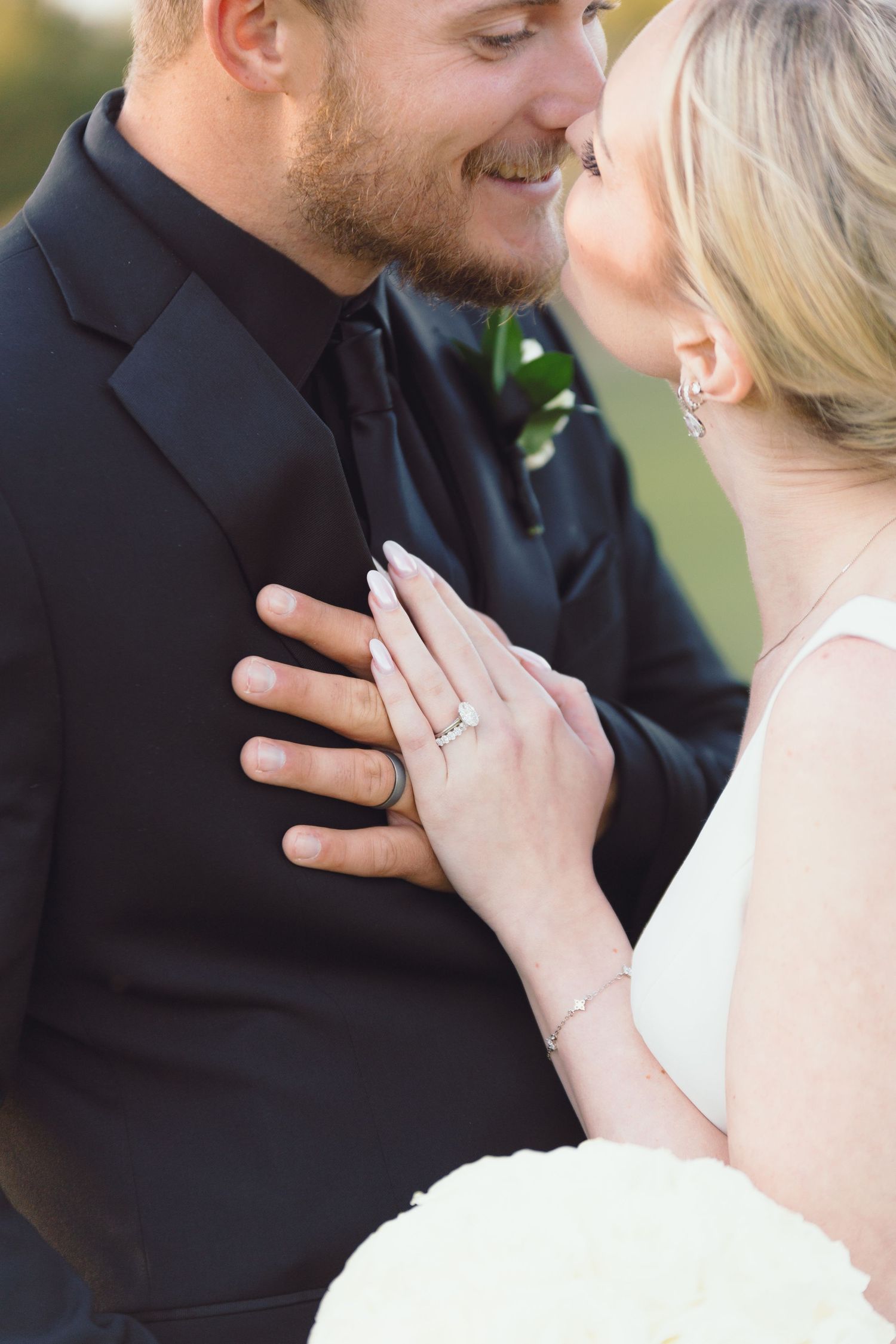 A smiling groom in black leans close to his blonde bride as she places her hand on his chest.