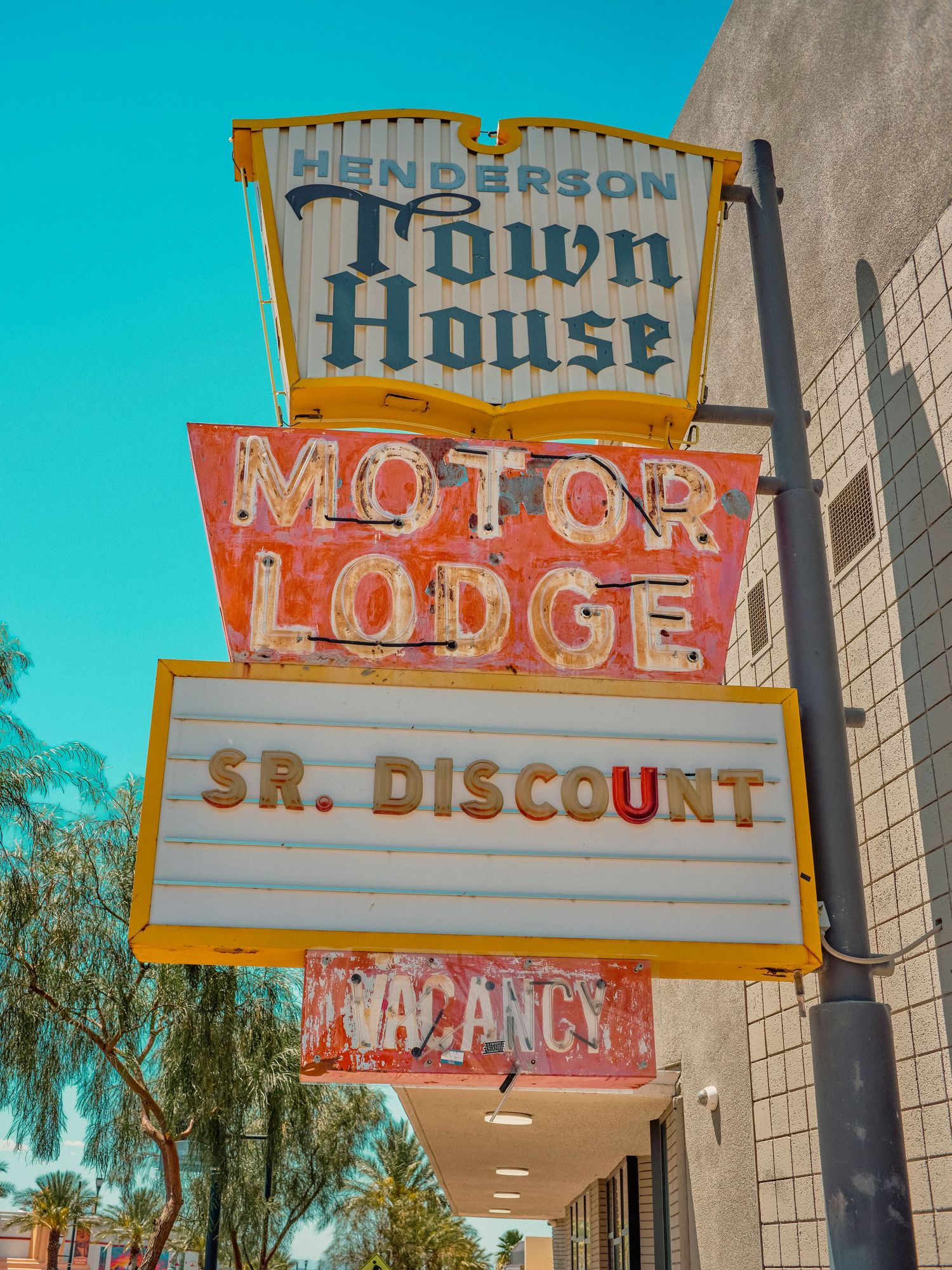 Vintage Henderson Town House Motor Lodge neon sign with Sr. Discount and Vacancy panels against a clear blue sky.