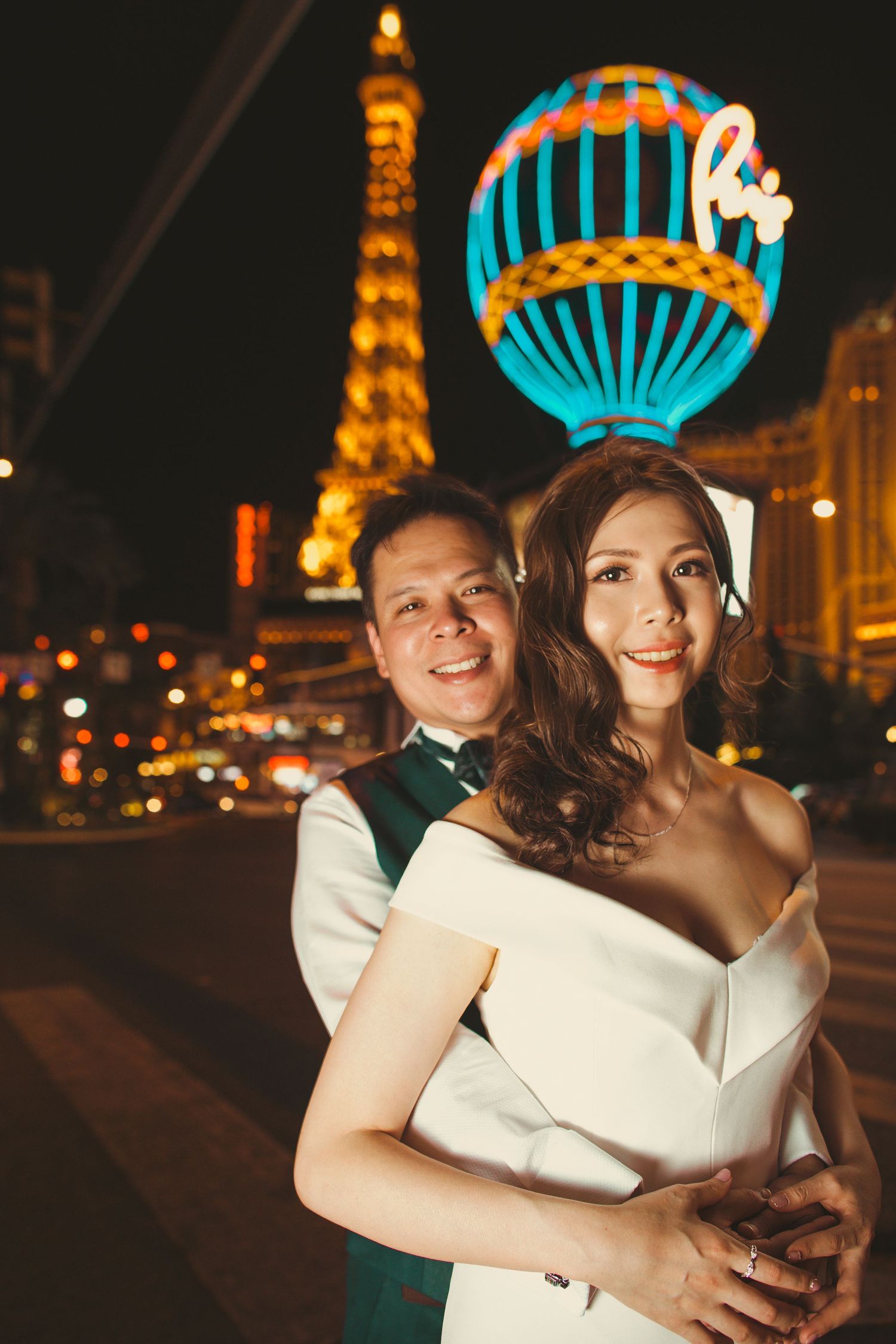 Bride and groom embracing on the Las Vegas Strip at night with Paris Hotel Eiffel Tower lit up behind them.