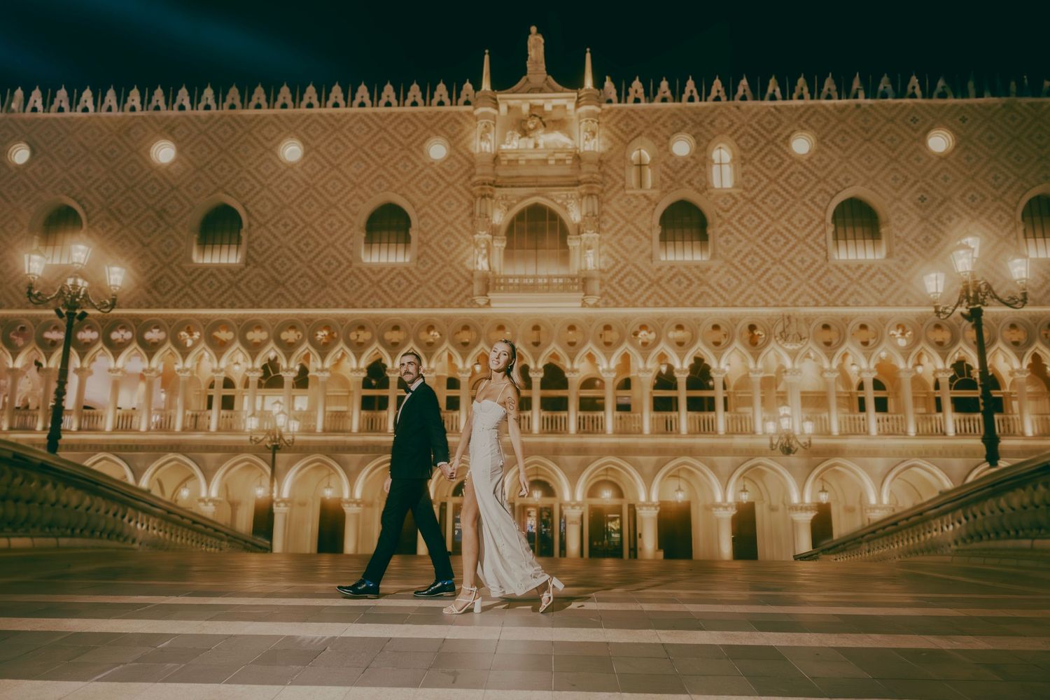 Elegant bride and groom strolling in front of The Venetian Las Vegas illuminated at night.