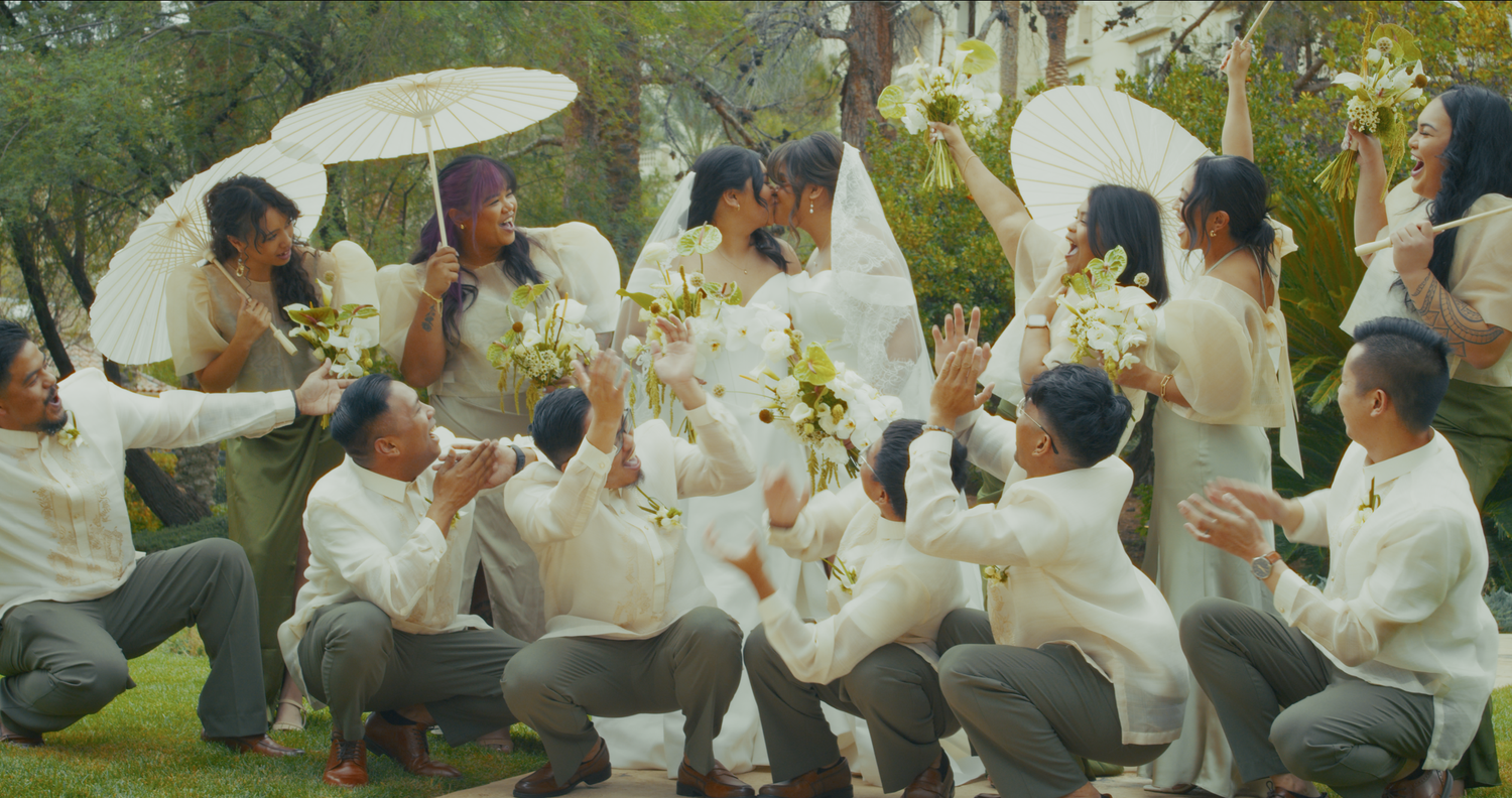 Wedding party in white attire celebrates outdoors tossing bouquets joyfully in a garden.