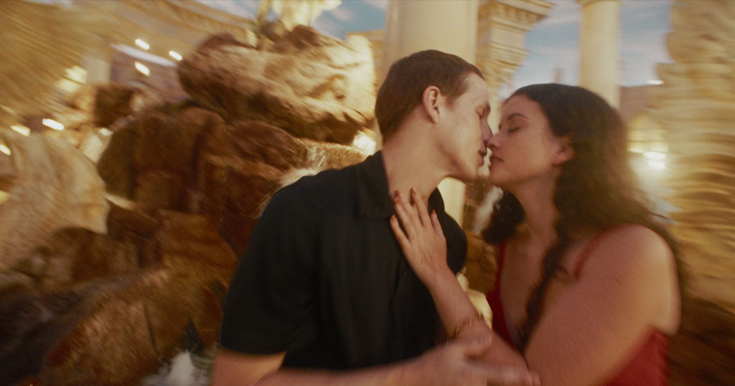 Couple sharing a passionate kiss near ornate stone fountain at a Las Vegas resort.