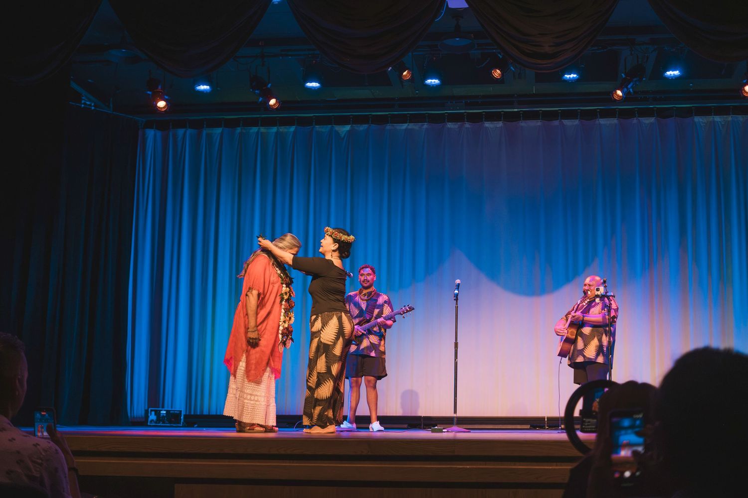 Colorful theatrical performers in costumes on a blue-lit stage during a live show performance.