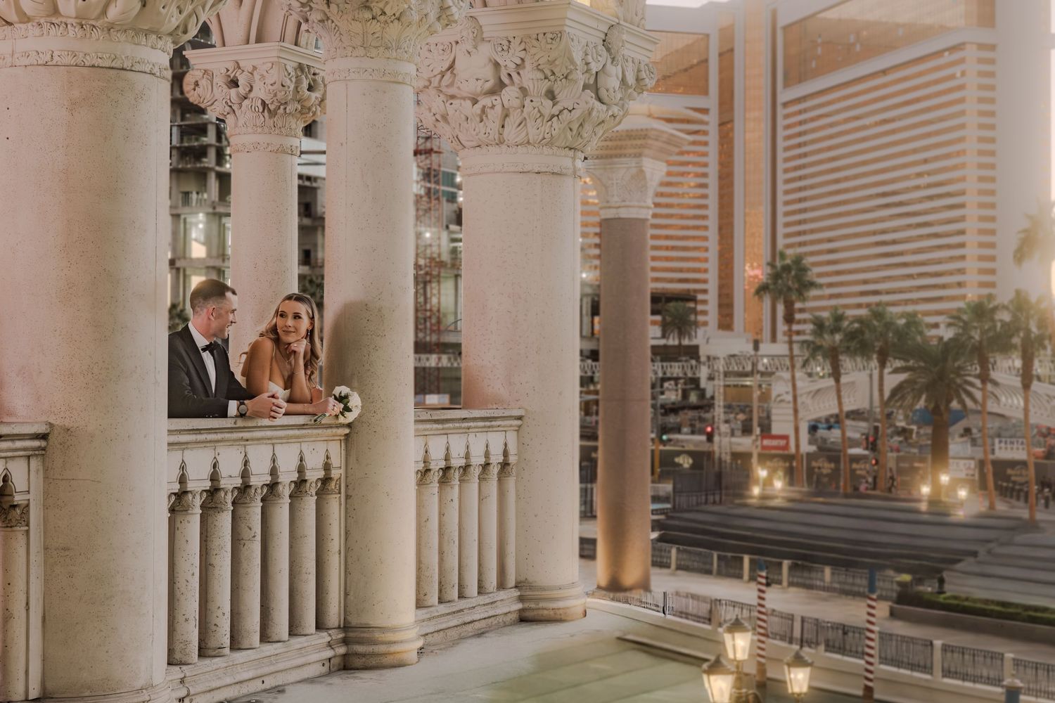 Bride and groom share romantic moment on elegant balcony overlooking Las Vegas Strip at dusk.