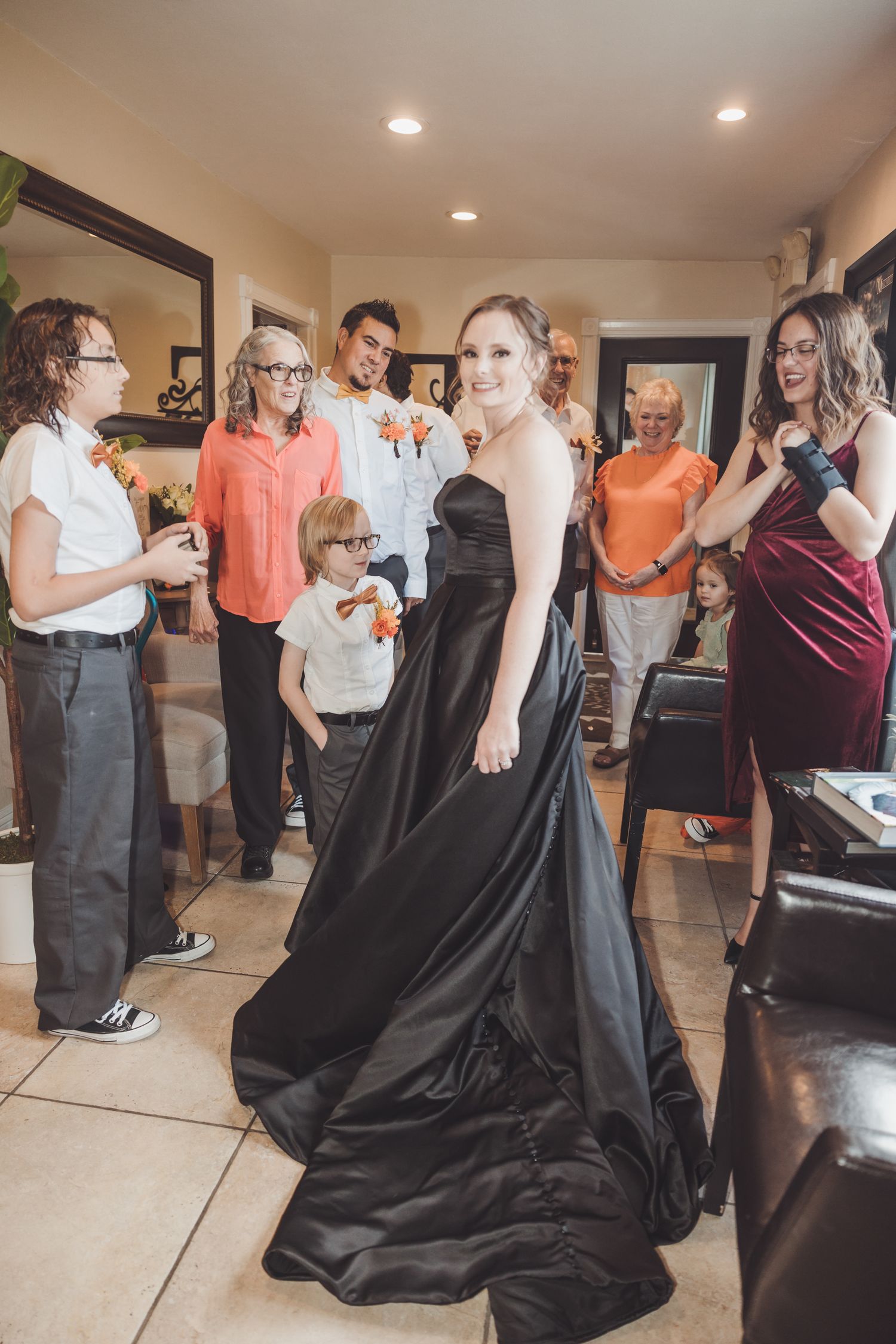 Bride in stunning black strapless wedding gown with long train surrounded by smiling wedding party indoors.
