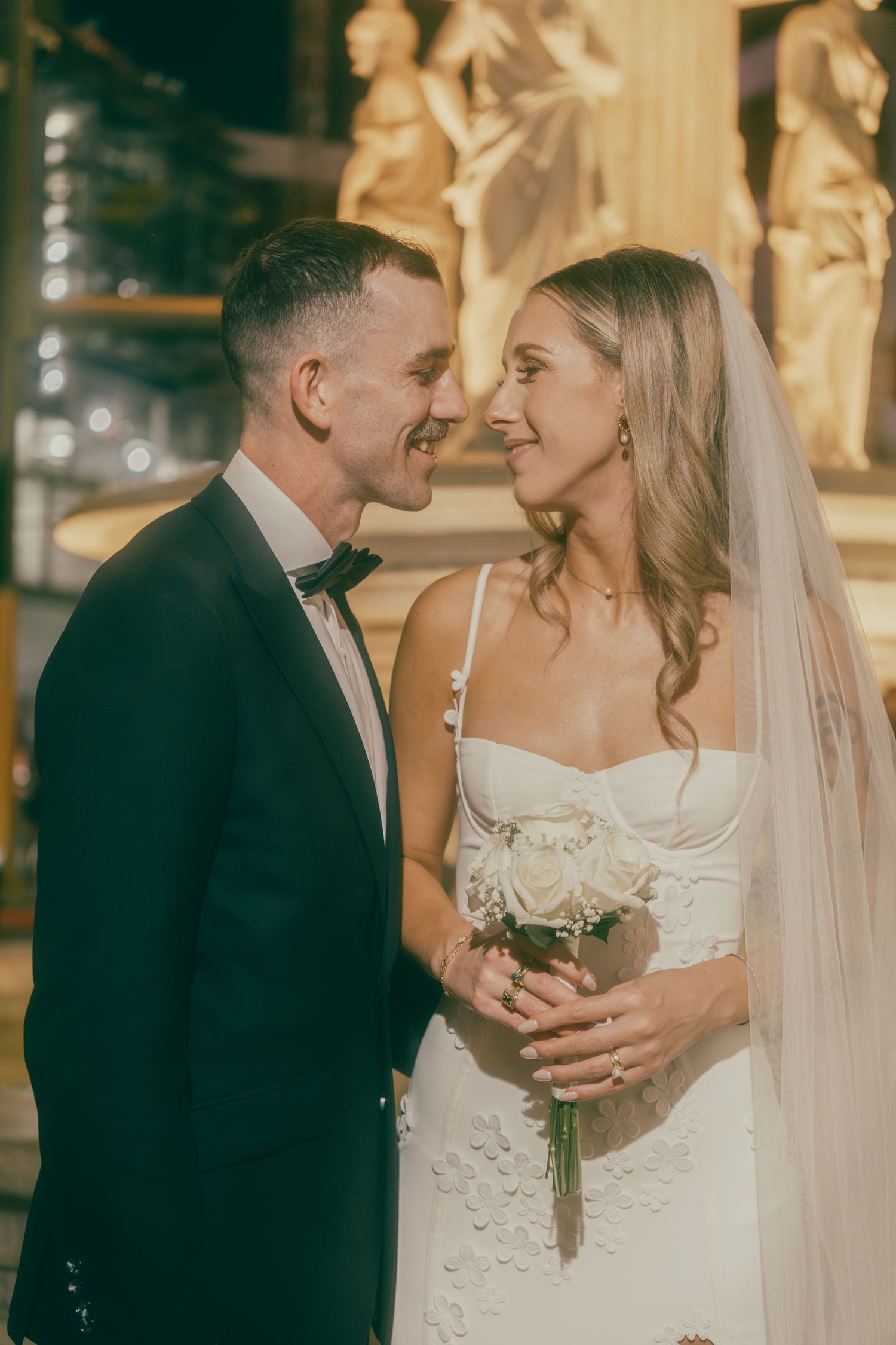 Smiling newlyweds touch foreheads romantically, bride in white veil holding white roses at Las Vegas venue.