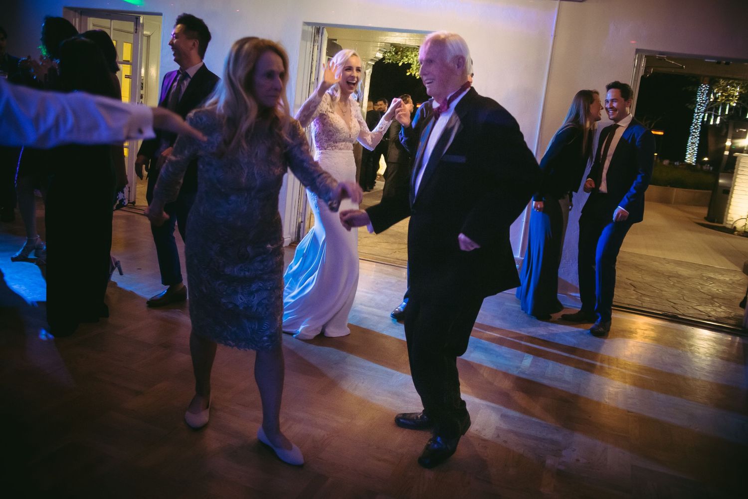 Elderly couple dancing together at a wedding reception on a wooden dance floor.