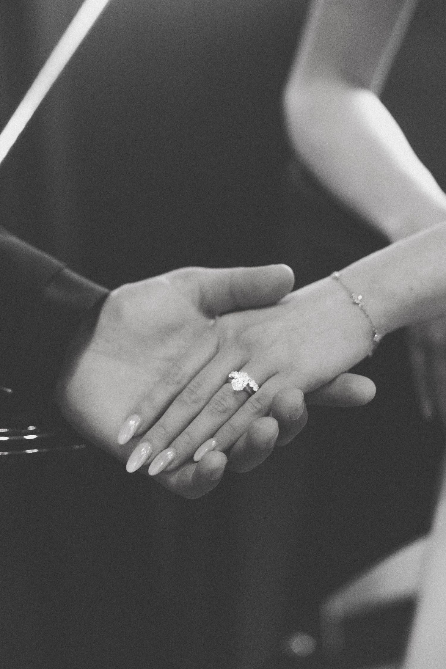 Close-up black and white photo of a couple holding hands, showcasing a diamond engagement ring.