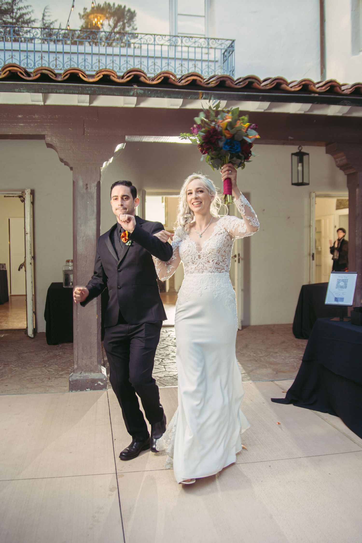 Bride in lace gown and groom in black suit making a joyful grand entrance at their wedding reception.