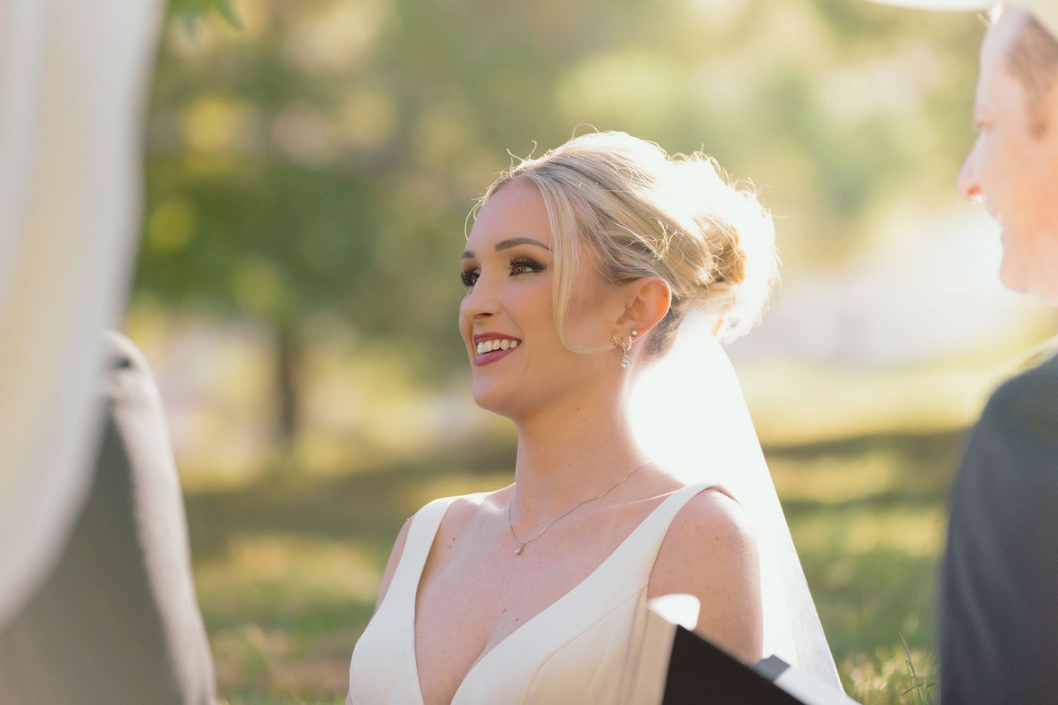 Smiling bride in white gown and veil during outdoor wedding ceremony.