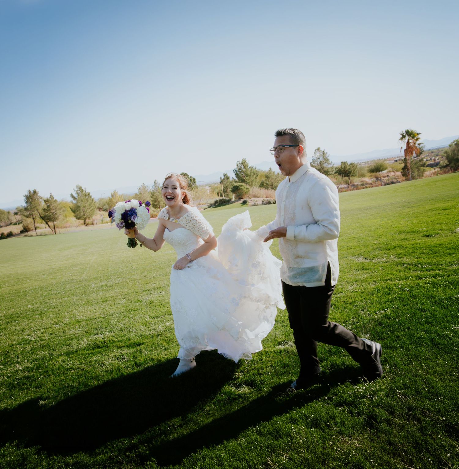Bride and groom walking on lush green golf course lawn on sunny wedding day, bride holding bouquet in white gown.