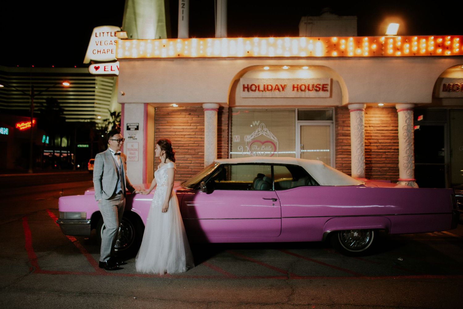 Bride and groom pose beside a pink Cadillac at night outside the Holiday House in Las Vegas.