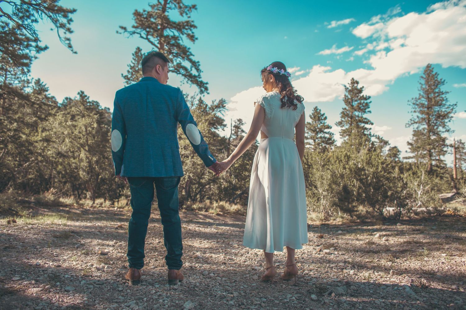 Bride and groom holding hands walking through pine forest on their outdoor wedding day.