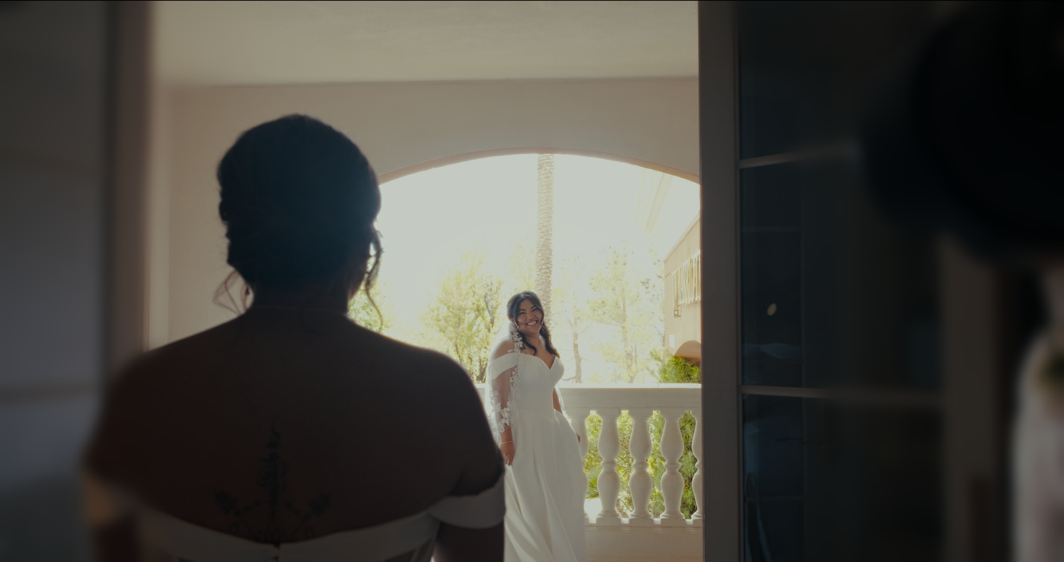 A bride in a white dress stands in an arched doorway viewed from a distance.