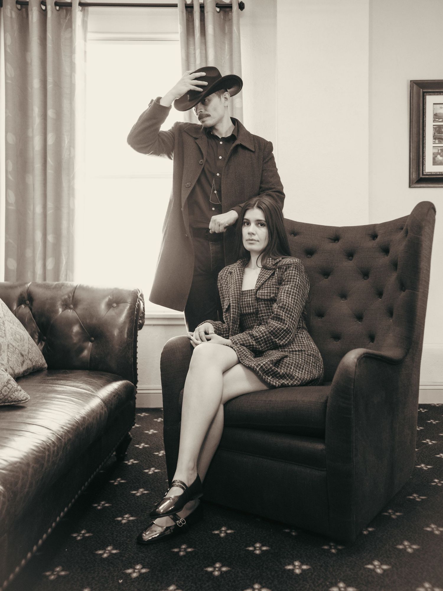 A man in a cowboy hat and woman in plaid dress pose in a vintage sepia-toned photo in an elegant room.