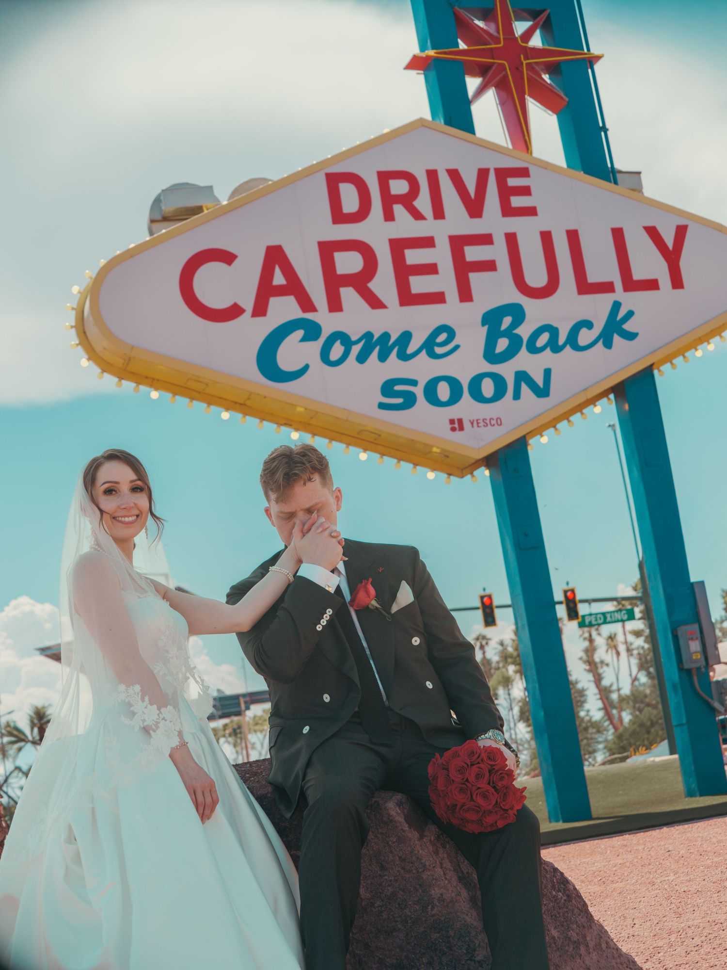Bride and groom posing in wedding attire before the iconic Las Vegas Drive Carefully Come Back Soon sign.