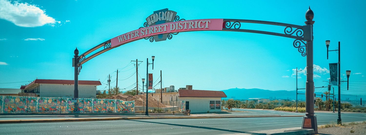 Decorative metal arch gateway marking the historic arts district entrance under a bright blue sky in a small southwestern town.