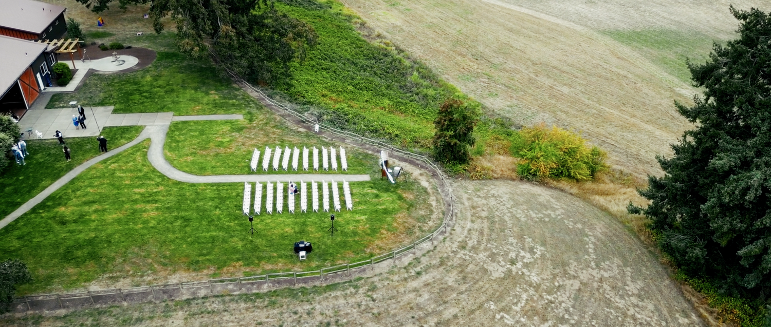 Aerial view of outdoor wedding ceremony setup with white chairs in field.