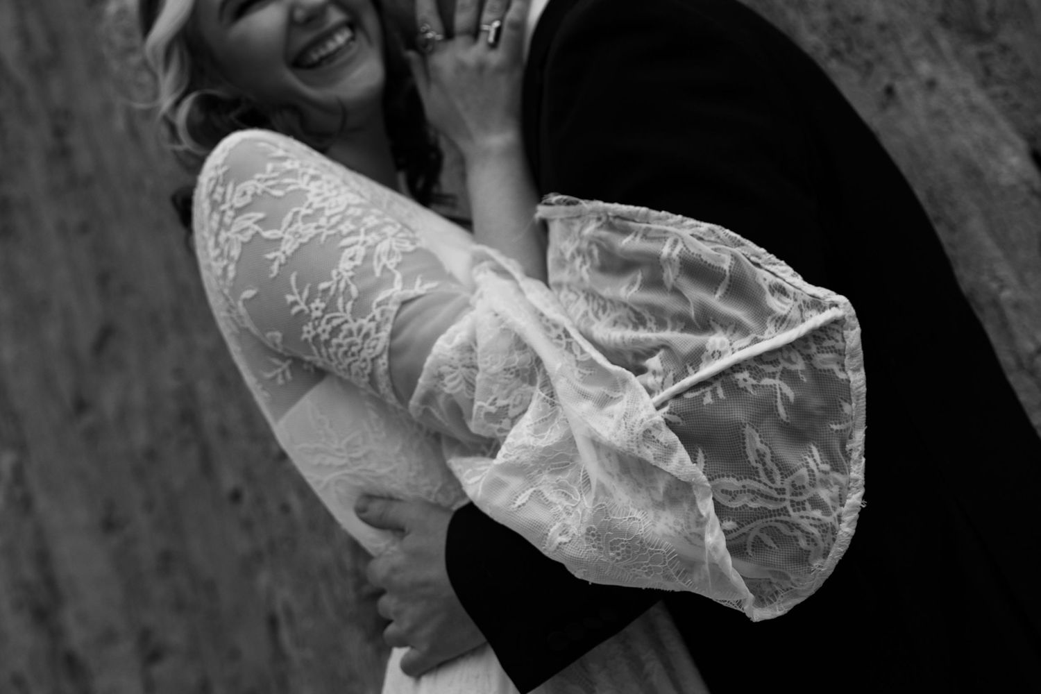 Black and white photo of bride and groom embracing, showcasing brides lace sleeve wedding dress.
