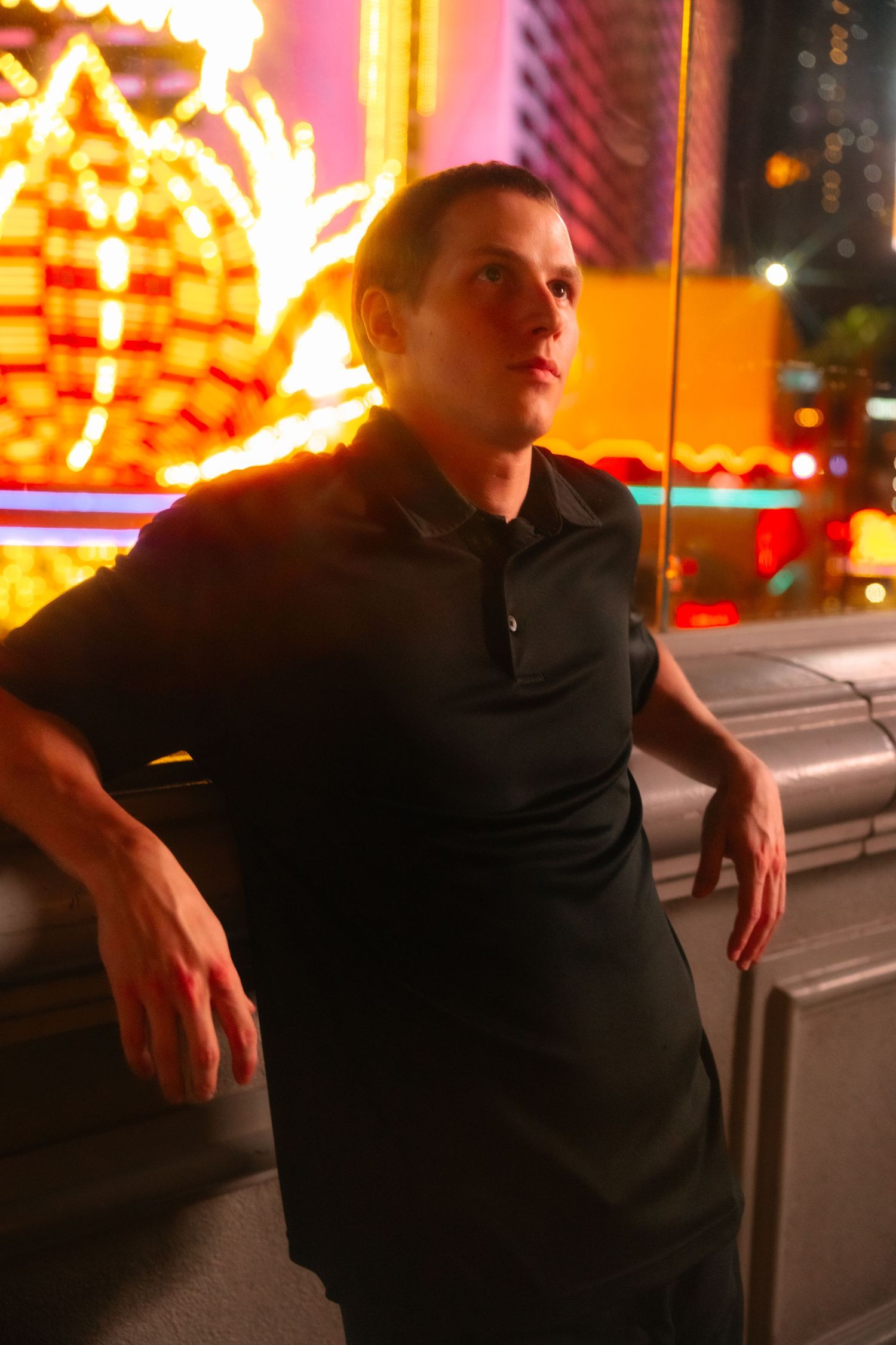 Person in black polo shirt leaning against railing with colorful neon lights in Las Vegas at night.