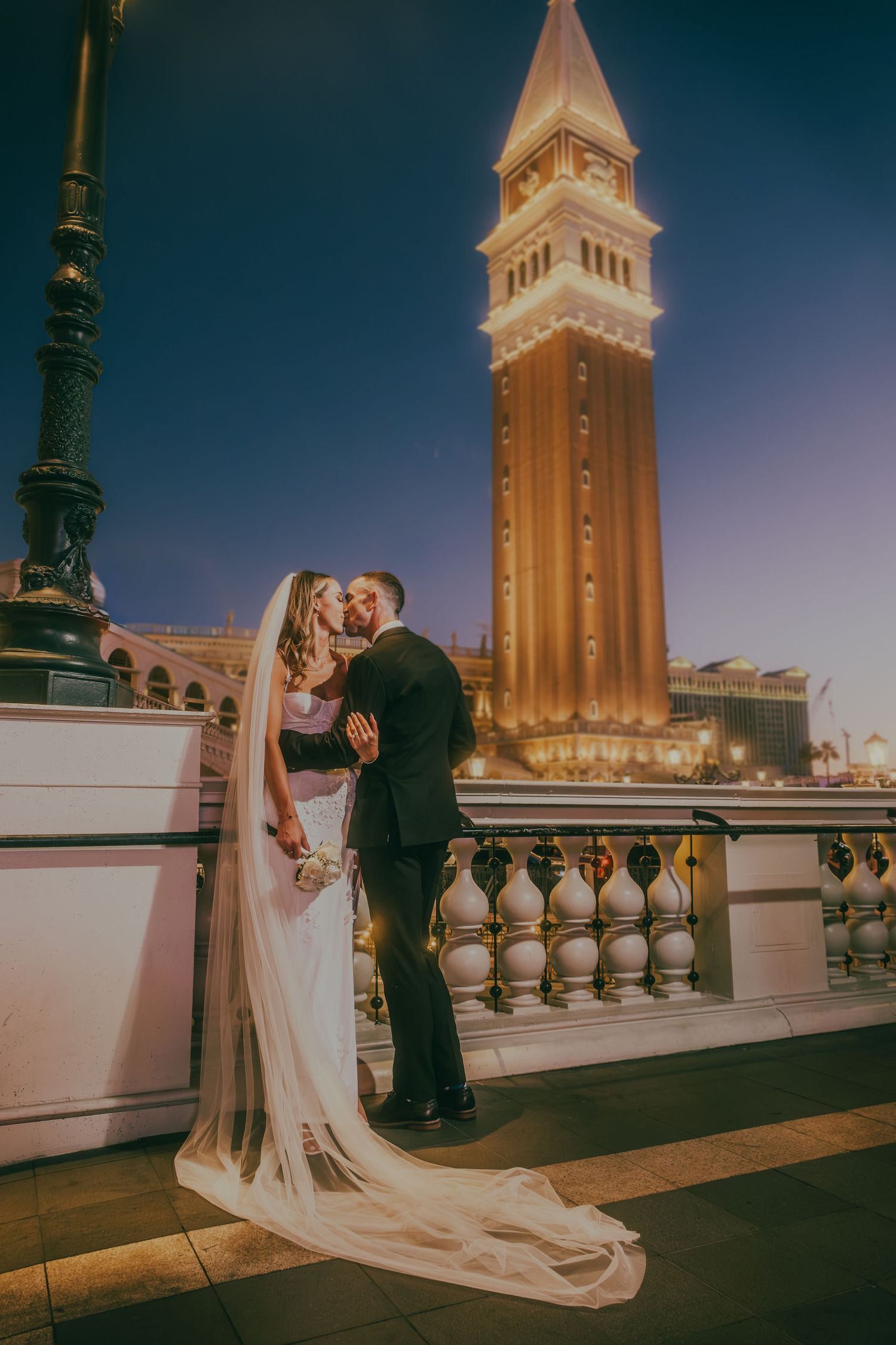 Bride and groom share a kiss with the iconic Venetian tower glowing behind them at night in Las Vegas.