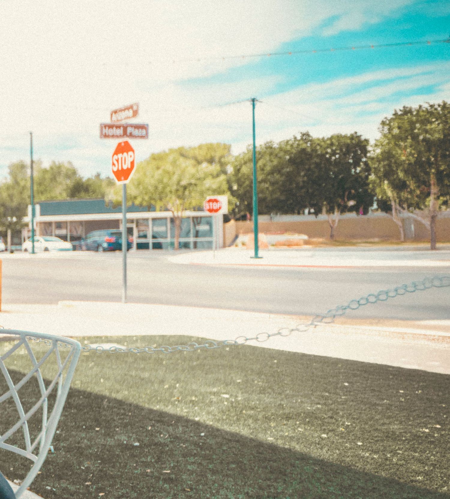 A sunny intersection with a stop sign, street signs, and trees near a small commercial building under a blue sky.