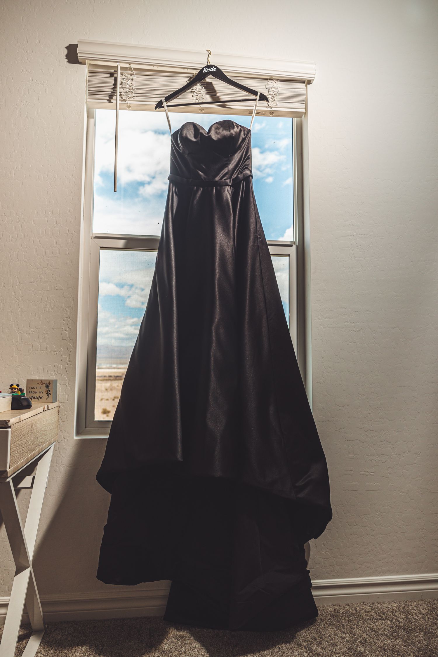 Elegant black strapless ball gown hanging on a window hanger, showcasing a sweetheart neckline and full skirt.