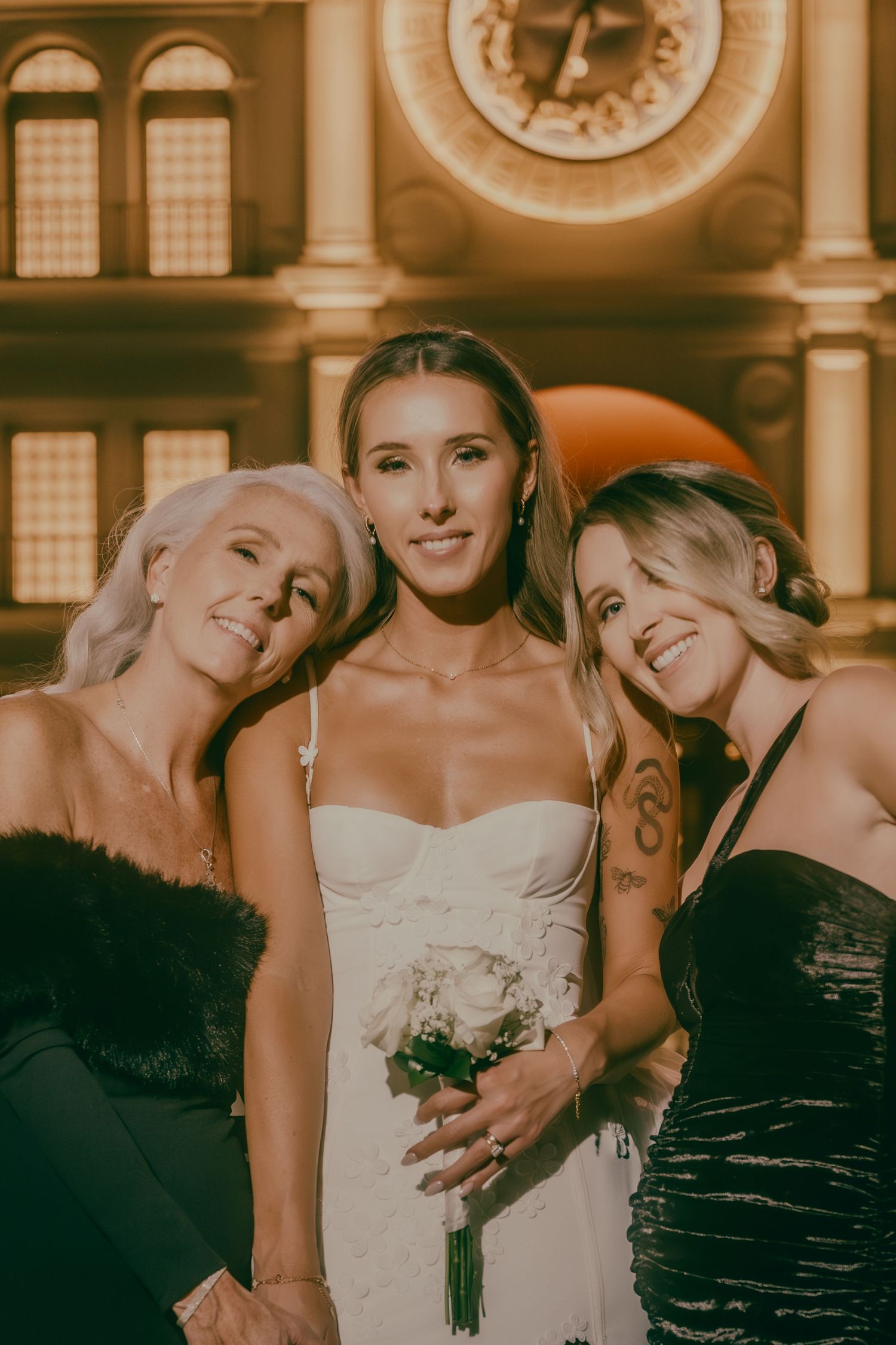 Smiling bride in white strapless gown laughs with two women in black dresses at Las Vegas wedding.