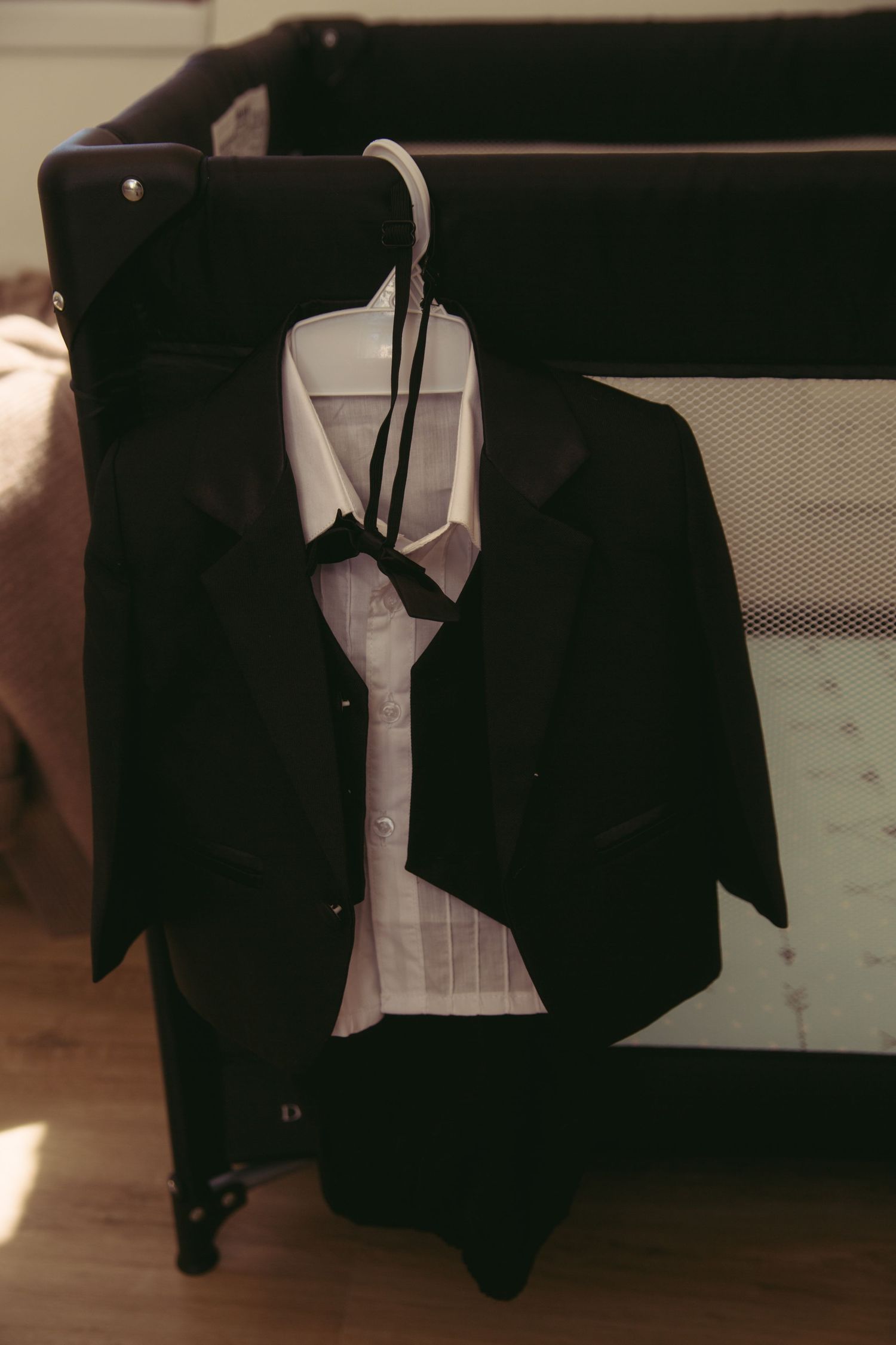 Black suit jacket and white dress shirt hanging on a hanger over a baby crib.