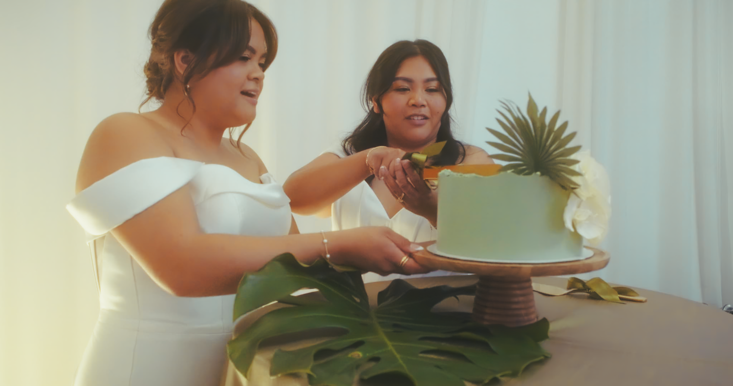 Two brides cutting a tropical-themed green wedding cake together.