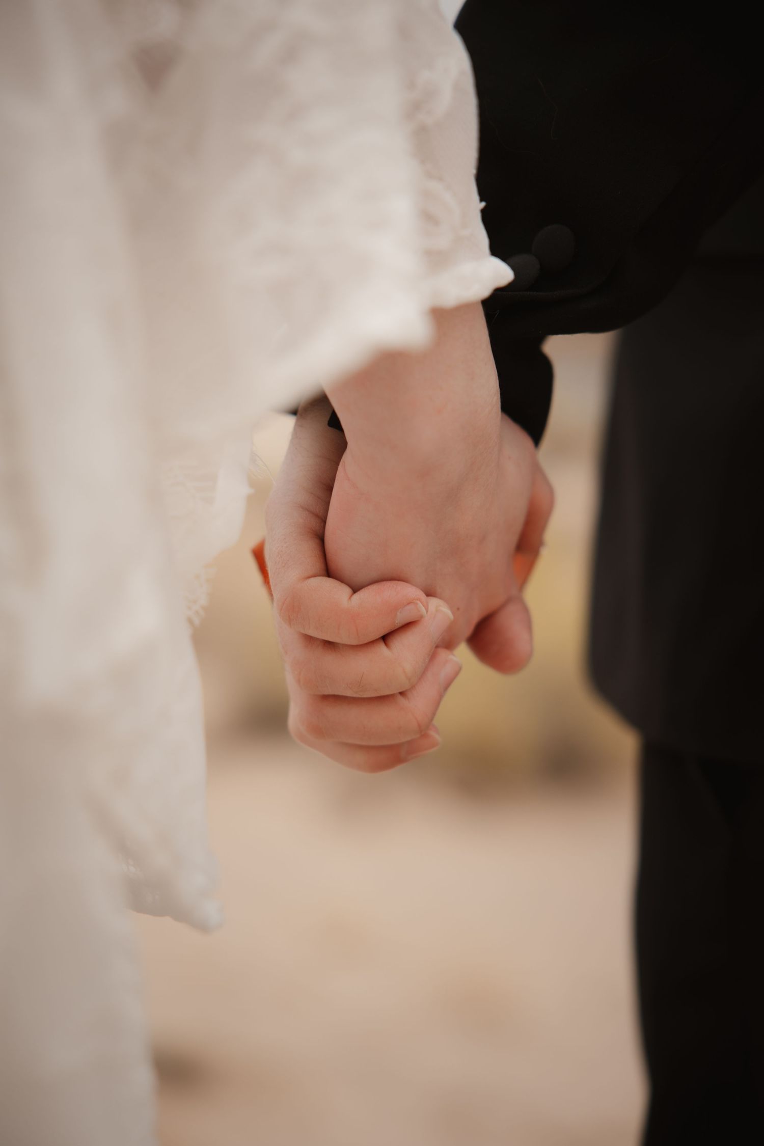 Close-up of bride and groom holding hands, showing lace wedding dress sleeve and black suit sleeve.