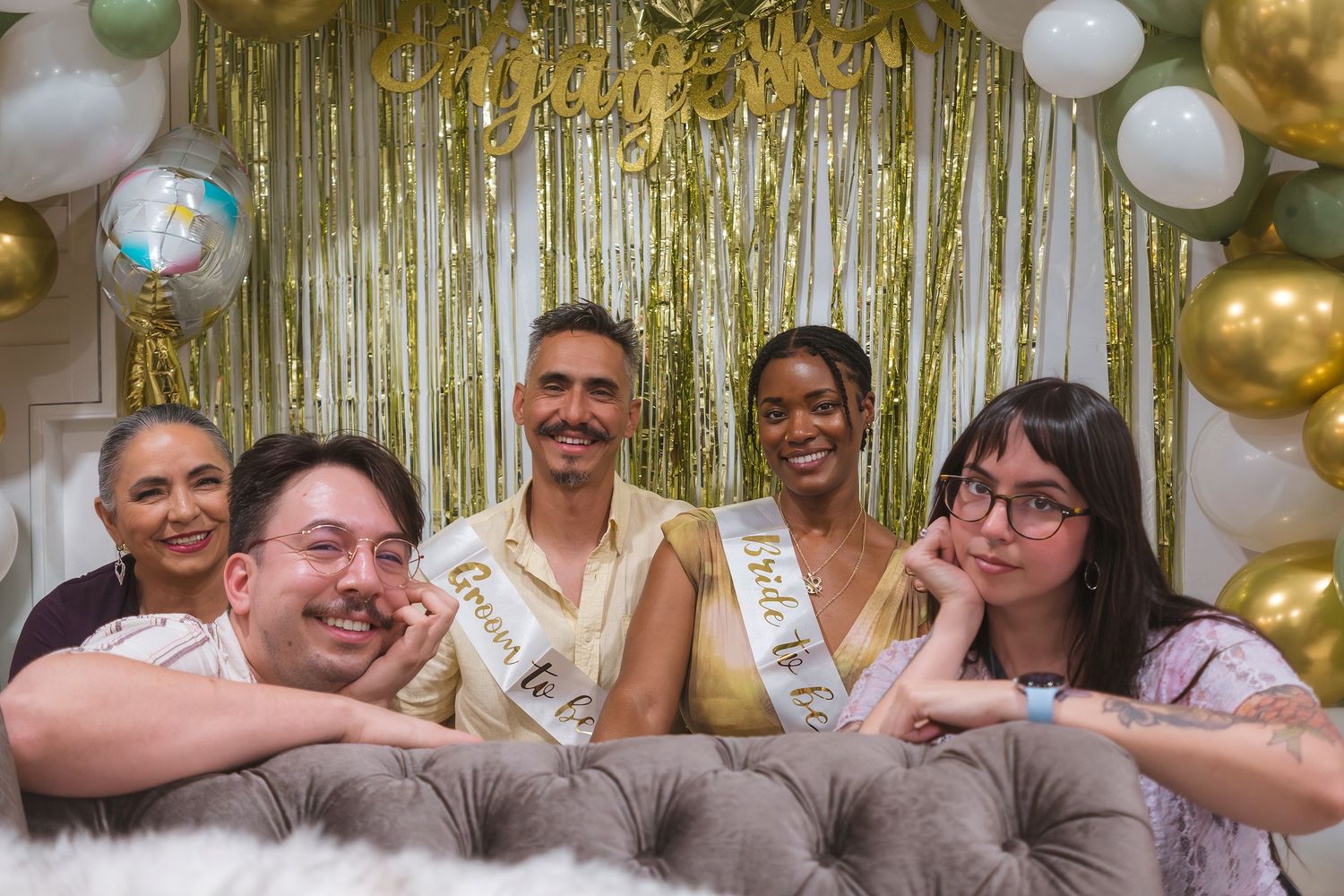 Group of five friends posing together at a festive party with gold streamers and balloon decorations.